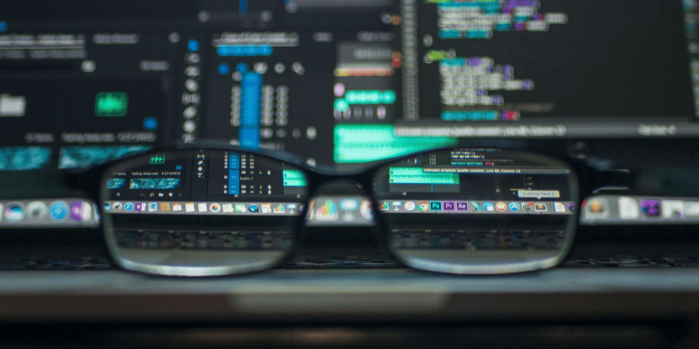 Two screens of code with a pair of glasses in front of them to illustrate that software verification is about looking at code.